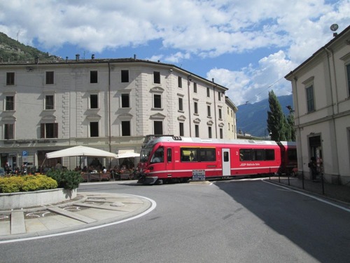 Tirano: trať č.950 regionalny vlak prechádza kruhovou križovatkou za bazilikou 